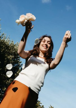 Mutlu genç bir kadın güneşli bir günde dışarıya gül yaprakları fırlatıyor.