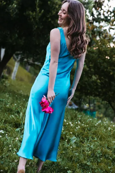 Bahçede çiçekleri tutan turkuaz elbiseli neşeli bir kadın.