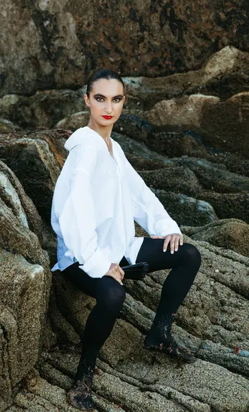 Deniz kenarındaki kayaların arasında oturan zarif genç dansçı.