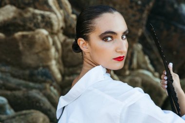 Cesur makyajlı flamenko dansçısı yelpaze tutuyor ve deniz kenarındaki kameraya bakıyor.