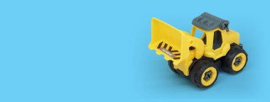 Sarı plastik buldozer oyuncağı mavi arkaplanda izole edilmiş oyuncak mağaza afişi için kopyalama alanı ile