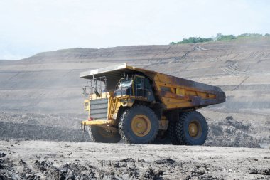 Eski, paslı, sarı maden kamyonu iş başında, kömür taşıyor.