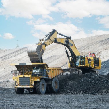 Taş ocağında çalışan büyük sarı maden kamyonu ve kazıcı. Kamyona kömür yükleniyor.