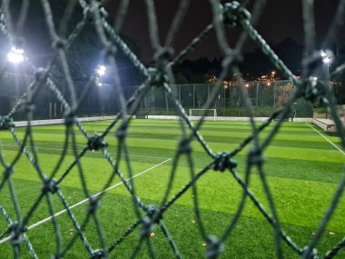 Futbol sahası ya da suni çimlerle kaplanmış sahada. Geceleri spor kompleksi sahasının arkasında..