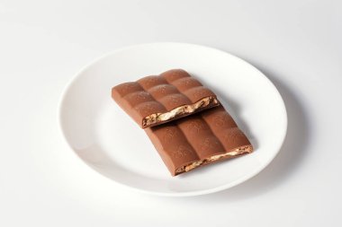 Beyaz arka planda sütlü çikolata. Çikolata beyaz tabakta parçalanmış.