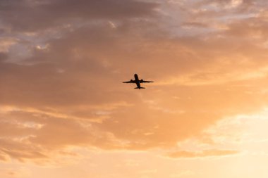 Gün batımında gökyüzünde uçan uçağın silueti.