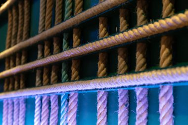 Soyut bir dekorasyon olarak duvarda asılı duran çapraz ipler. Ev yapımı, yeşil arka planı ve renkli ışıkları olan orijinal bir iç tasarım. Halatlar doğal elyaf. Boyutları oldukça büyük.