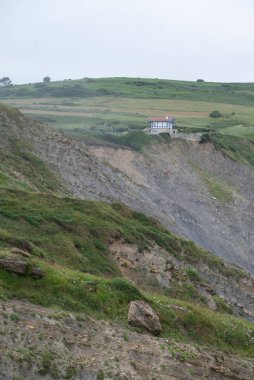 Uçurumun kenarındaki ev. Bask bölgesindeki Bilbao yakınlarındaki Flysch 'tayız. Fotoğraf yağmurdan hemen sonra çekildi, rüzgarlı bir günde dalgalı deniz ile..