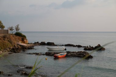 Yunanistan 'da sabahın erken saatlerinde sakin bir deniz manzarası ve gökte kümülüs bulutları olan bir morina burnu yarımadasına yakın bir tekne..