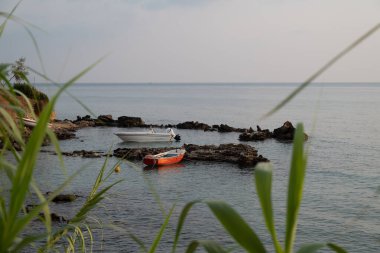 Early morning scene in Greece, with tranquil sea and a boat moored in silhouette close to a cape cod peninsula with cumulus clouds in the sky. clipart