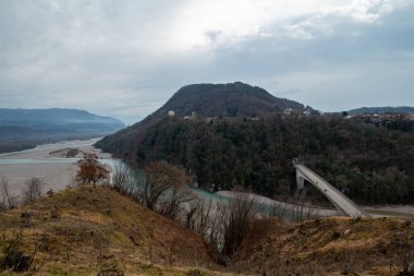 The bridge to Pinzano al Tagliamento, the city is sitting on a hill top. We see the riverbed underneath in a quiet foggy morning of winter clipart