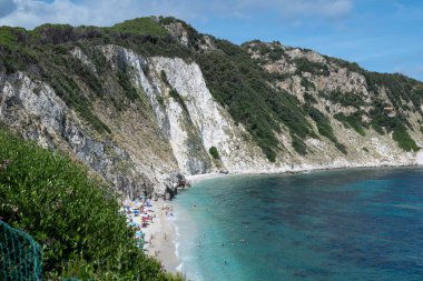 Yazın Elba Adası 'ndaki Sansone Sahili' nde güneşli yataklar ve güneş şemsiyesi ile deniz kıyısında birçok banyo ve yüzme.