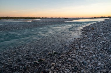Tagliamento nehir yatağı alacakaranlıkta kayalar, çakıl taşları ve güneş ışınları ipek gibi tatlı sulara uzun süre yansıyor.