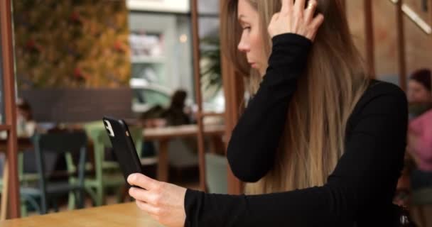 都会のコーヒーショップのスタイリッシュな女性は ミラーアプリと髪を修理する電話画面を使用しています ファッショナブルな女性大人はレストランのテーブルに一人で座り 彼女の視点を世話します 高品質の4K映像 — ストック動画