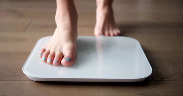Young girl teenager steps on white scales to measure control weight. Teen checks body mass and fat, healthy dieting and fitness concept. High quality photo