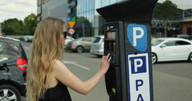 Park sayacında güneş gözlüklü ve elbise plakalı bir kadın var. Zarif nesil z kadın sürücüsü park bileti almak için park yerindeki tuş takımı tuşlarına basıyor.