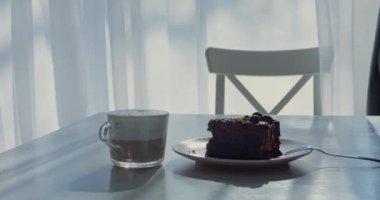 Kadın eli bir fincan kapuçino ya da latte kahve ve kek alır. Parlak yaz güneşli bir günde perdeli pencerenin yanında telefonsuz güzel bir sabah rutini. Yüksek kalite 4k görüntü