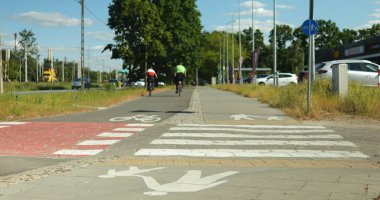 Soluk ve asfaltlı bisiklet yolu ve beyaz boyalı yaya yolu tabelaları. Kentin varoş bölgesinde karayolu boyunca özel bisiklet yolu ve yaya yolu altyapısı