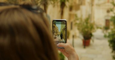 Yakın çekim kadın el kamerası akıllı telefon Kadim caddedeki fotoğraf binasını çekiyor. Ortaçağ şehir merkezinde kamera ile turistik çekim yapan yüzü olmayan kadın turist. Yüksek kalite fotoğraf