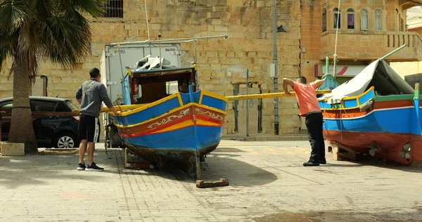Marsaxlokk, Malta - 1 Mayıs 2023 - İki balıkçı ağaç kütükleri ve manuel güç kullanarak renkli Marsaxlokk teknesini römorka yüklemeye çalıştı.