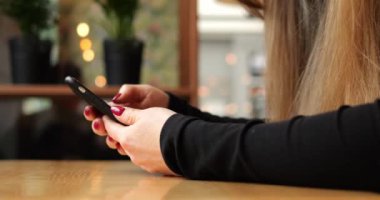 Kadın kolunu kapat akıllı telefon kamu binasının içindeki ahşap masada uzan. Uzun kahverengi saçlı, siyah uzun kollu, cep telefonlu, kırmızı ojeli kimliği belirsiz bir kadının elleri..