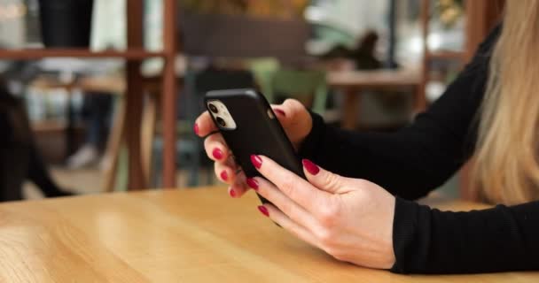赤いネイルポーランドのクローズアップショット女性指は カフェで携帯電話の画面を操作します 長い茶色の髪を持つ認識できない女性大人は テーブルに座り スマートフォンアプリケーションを使用しています 高品質の4K映像 — ストック動画