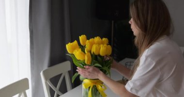 Genç ve güzel bayan, parlak sarı lale aromasını seviyor. Romantik kokular, evde atmosfer, bant ve fiyonkla dekore edilmiş cam vazo. Yüksek kalite 4k görüntü
