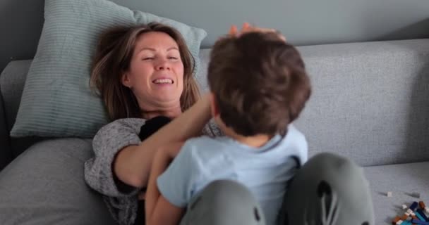 若い母親は5歳の息子を家でソファーで笑った 週末の幸せな家族の時間 子供と遊ぶ親の本当の感情 高品質の4K映像 — ストック動画