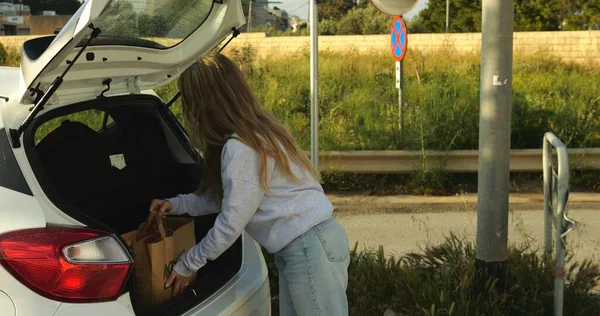 Genç bir kadın, araba bagajında satın alınabilecek çevre dostu geri dönüşümlü kağıt torba taşıyor. Çevresel farkındalığı olan yetişkin bir kadın, alışveriş için biyolojik olarak ayrıştırılabilir ambalajı kullanmayı bilinçli bir şekilde seçiyor. 4k görüntü