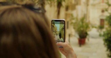 Yakın çekim kadın el kamerası akıllı telefon Kadim caddedeki fotoğraf binasını çekiyor. Ortaçağ şehir merkezinde kamera ile turistik çekim yapan kadın turistin suratsız fotoğrafı. 4k görüntü