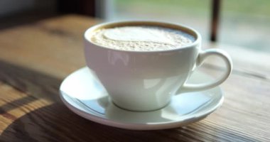 Taze kahve, seramik bardakta krema ve ahşap masa üzerinde yakın plan. Sabah enerjiyi patlatmak için yeni demlenmiş romatik içecek. Kahve servisi.