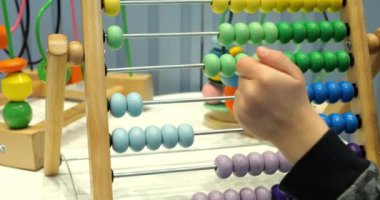 Küçük öğrenci, anaokulunda abaküs ve renkli boncuklar kullanıyor. Küçük çocuk matematik dersi sırasında oyuncakla oynuyor. Çocuk gelişimi