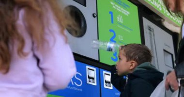 Küçük çocuk kullanılmış plastik şişeyi şehir caddesinde ters satış makinesine koyuyor. Küçük çocuk çevreyi korumak için çöpleri ayırıyor. Sürdürülebilir hayat