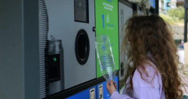 Uzun kıvırcık saçlı küçük kız plastik şişeyi şehir caddesinde ters satış makinesine koydu. Çocuklara her gün çöp toplamayı öğretiyorum.