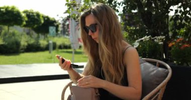 Sarışın kadın şehir parkında makyaj yapmak için aynaya bakar. Güzel bayan ayarları açık kafe terasında yansıma kullanarak görünür.