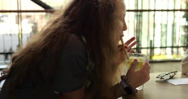 Uzun, gevşek saçlı genç kız kafedeki masada samandan limonata yudumlamayı seviyor. Dişi çocuk yüzü yoğun ekşiliğe tepki olarak kıvrılır.