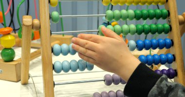 Küçük öğrenci, anaokulunda abaküs ve renkli boncuklar kullanıyor. Küçük çocuk matematik dersi sırasında oyuncakla oynuyor. Çocuk gelişimi