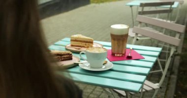 Masada latte ve cappuccino içen bir kadın ve açık havada kek çeşitleri. Kafe, kadın vejetaryenlere özel diyet uygulamayı güvence altına alıyor.