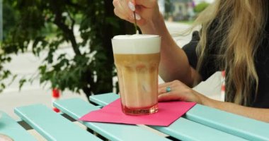 Kadın sütsüz sütlü sütlü latte 'yi kafe yazlığında usulca karıştırıyor. Bayan, içkinin vejetaryen diyeti ile aynı hizada olduğunu bilmek hoşuna gidiyor.