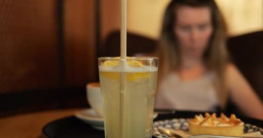 Taze limonata bardağı, kremalı tart ve kahve. Kadın, kafede lezzetli tatlı ve içki sipariş ediyor. Turunçgil içeceği tazeleniyor