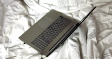 Yatak odasına beyaz buruşuk battaniyeyle yerleştirilmiş uyku modunda güçlü bir laptop. Esnek program rahat bir atmosferde çalışma olanağı sağlar