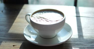 Kapuçino, seramik bardakta köpükle kapuçino, parlak sabah ışığı altında ahşap masada. Kahve dükkanında servis edilen taze kahve. Enerji içeceği.