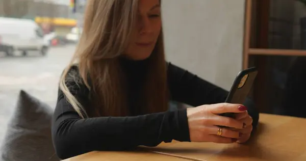 Genç bir kadın akıllı telefon ekranında yazı yazıyor ve restoranda oturmuş gülümsüyor. Kadın müşteri sosyal medyada zaman geçirir ve geçirir, haberlere bakar ve tepki verir ve yorumlara ve mesajlara cevap verir. 4k