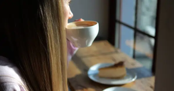 Kadın, güneşli bir sabahta kafenin penceresinin yanında otururken küçük bir yudum kahve içer. Kadın, şehrin klasik kahve dükkanında kafeinsiz içecekten hoşlanıyor.