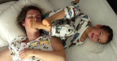 Pijamalı şirin bir çocuk uyanıyor ve uyuyan annesinin üzerinde yuvarlanıyor. Aktif küçük oğlu sabah oynarken genç bir kadın kestiriyor.
