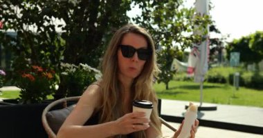 Bayan kafe ziyaretçisi parkta yaz terasında hamur işleriyle servis edilen kahveyi rahatça içiyor. İş kadını molada sokak kafesinde öğle yemeği yiyor.