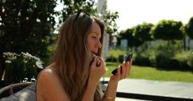 Genç bir kadın parktaki kafe terasında rujla dudak boyuyor. Doğaçlamanın yardımıyla hızlı bir makyaj. Bayan yürürken makyajı düzeltir.