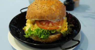 Çırpılmış yumurtalı lezzetli burger taze marul ve sulu domates dilimi. Ağız sulandıran burger. Susamlı çöreğin arasına sıkıştırılmış. Mükemmel bir ikram.