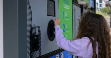 Küçük kız, şehir caddesinde ters satış makinası gösteriminde seçenekleri seçmek için tuşa basıyor. Atık maddeleri sürdürülebilir teknoloji ile yeniden kullanmak