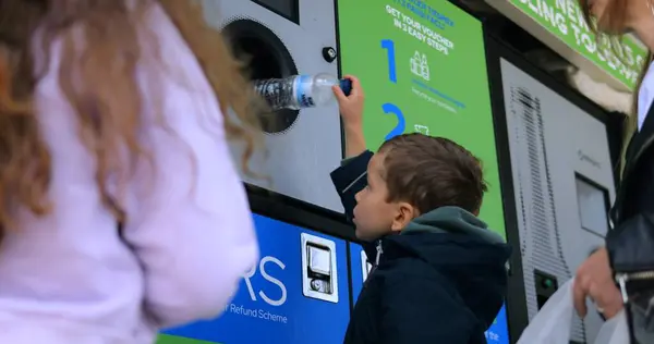 Küçük çocuk kullanılmış plastik şişeyi şehir caddesinde ters satış makinesine koyuyor. Küçük çocuk çevreyi korumak için çöpleri ayırıyor. Sürdürülebilir hayat